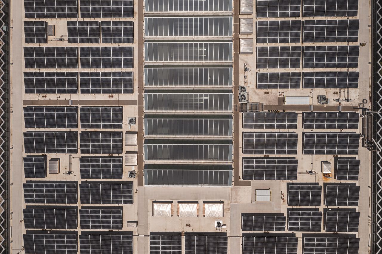 services-03 A high-angle drone shot capturing a grid of solar panels on a large industrial rooftop, showcasing renewable energy.
